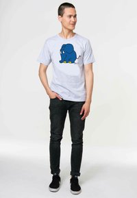 Gray short-sleeve t-shirt featuring a blue cartoon elephant with yellow accents. Worn with dark jeans and black sneakers.