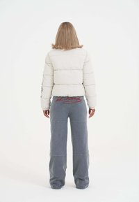 Donna con capelli biondi alla spalla che indossa un giubbotto bianco imbottito e pantaloni grigi larghi con ricami rossi "ed hardy" sul retro.