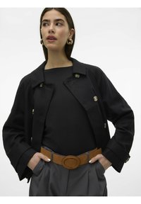 Giacca nera doppiopetto con design a colletto, con bottoni argentati. Indossata sopra una maglietta nera, abbinata a pantaloni grigi a vita alta e una cintura marrone.