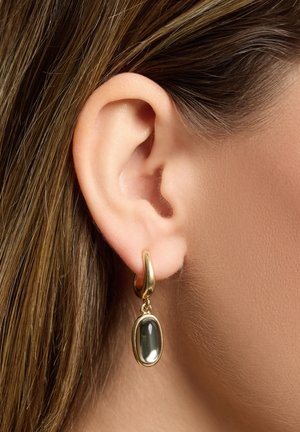 Goldene Creolen schmücken einen ovalen, dunklen Steinfentos. Das Design ist glatt mit reflektierenden Oberflächen, die den Kontrast zwischen den Materialien betonen.