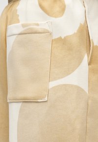 Tela beige con grandes patrones abstractos suaves en marrón y crema; cuenta con un bolsillo parche cosido en la parte frontal.