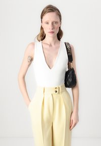 Valkoinen ilman hihoja bodysuit syvällä V-kaula-aukolla, pari korkeavyötäröisten keltaisten housujen kanssa, joissa on kaksi kultanappia. Pieni musta tikattu käsilaukku.