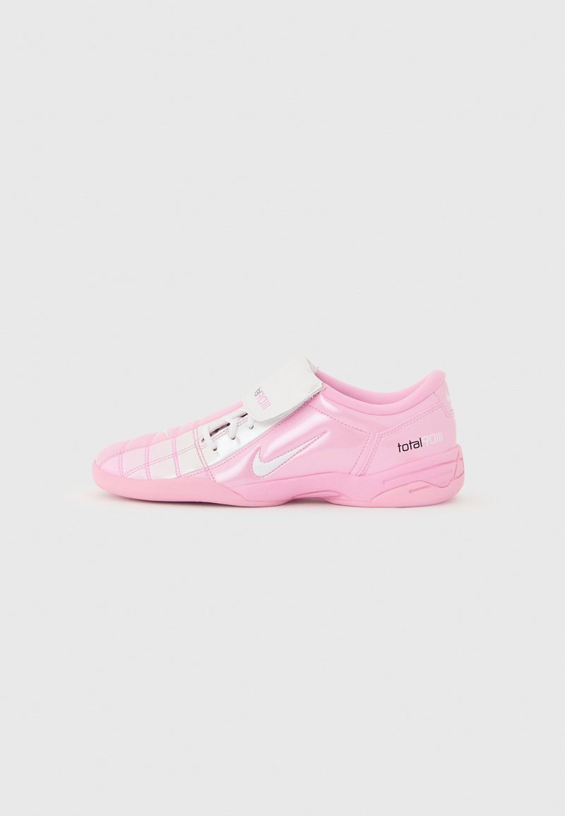 Ροζ και λευκό ποδοσφαιρικό παπούτσι Nike Total 90 III χαμηλού προφίλ με ασημί λογότυπο swoosh και επιπλέον χιαστί λουράκι πάνω από τα κορδόνια, σε απλό φόντο.