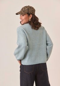 Suéter de punto texturizado en azul claro con hombros caídos y dobladillo acanalado. Combinado con jeans oscuros y una gorra de estampado de leopardo.