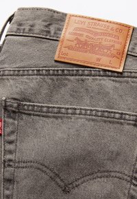 Acercamiento a un bolsillo trasero de unos jeans de denim gris con una etiqueta de cuero marrón de Levi Strauss & Co. y una pequeña etiqueta de tela roja en la costura lateral.