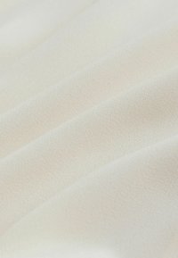 Tessuto bianco in una morbida trama testurizzata con un leggero lucido, caratterizzato da pieghe e drappeggi delicati che evidenziano la sua fluidità e leggerezza.