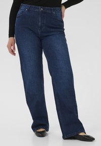 Mørkeblå jeans med vide ben lavet af denim, med fem lommer og knaplukning. Glat tekstur med diskrete syningsdetaljer langs sømmene.