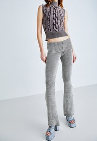 Stickad ärmlös topp med kabelmönster i grått och vitt, kombinerad med grå ribbstickade volangbyxor med sidoknappar och en bred midja.