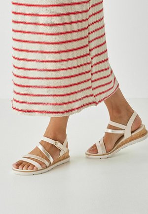 Világos bézs ék sarkú szandálok többféle texturált pánttal és parafa sarokkal. A talp fehér, pöttyözött mintázattal a tapadás érdekében.