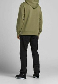 Felpa con cappuccio verde oliva, tessuto misto cotone, vestibilità rilassata, abbinata a jeans neri e sneakers nere con accenti bianchi.