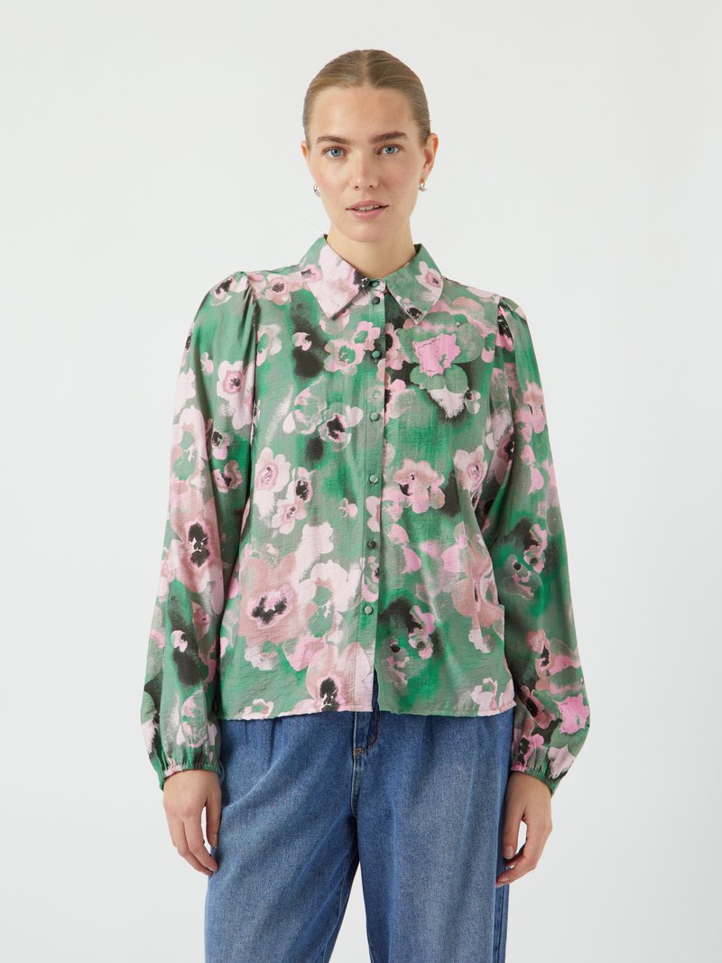 Vloeiende, groene bloemenblouse met roze en zwarte accenten, knoopsluiting aan de voorkant en opgeblazen mouwen. Zachte textuur en relaxte pasvorm, gecombineerd met denim.