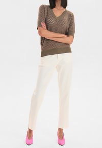 Top de punto marrón con escote en V y mangas cortas, combinado con pantalones crema y zapatos de tacón alto rosa brillante. Patrón texturizado sutil en el top.