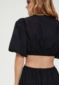 Must mustrindiga must cropped top puff varrukatega; valmistatud siledast kangast, millel on elastne vöökoht ja viimistletud õmblused, et saavutada istuv välimus.