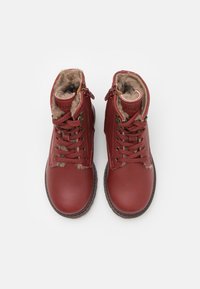 Bottines en cuir rouge avec doublure en fausse fourrure, lacets contrastants et fermeture éclair sur le côté. Bout rond et semelle en caoutchouc robuste.