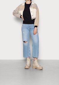 Avklippt, färgblockerat denimjacka i beige och brunt, kombinerat med en svart t-shirt, ljusblå vida jeans och beige klumpiga stövlar.