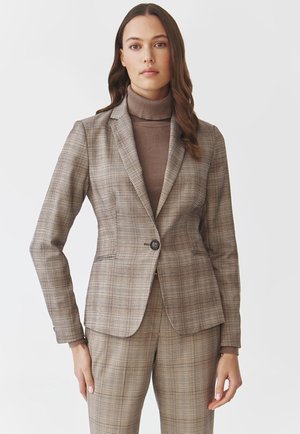 Hnědý kostkovaný blazer s přiléhavým střihem, jednořadým zapínáním na knoflík a klopami, kombinovaný s odpovídajícími kostkovanými kalhotami a hnědým rolákem.