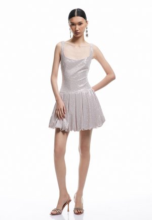 Abito mini lucido e aderente in rosa metallico con scollo quadrato e gonna a pieghe. La modella indossa orecchini argento e sandali con cinturini.