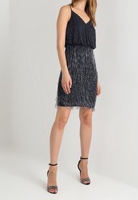 Vestido de marina con tirantes finos, con detalles de flecos texturizados por toda la prenda y una parte superior suelta y drapeada. Llevado con tacones negros de tiras.