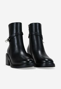 Botas de tobillo de cuero negro con un acabado suave, punta cuadrada y tacón grueso. Presentan una cremallera lateral elegante y una correa decorativa con una hebilla plateada.