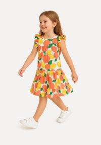 Gelbes Kleid mit orangefarbenen und zitronenartigen Mustern, mit Rüschensleeves und einem ausgestellten Rock, kombiniert mit weißen Sneakers.