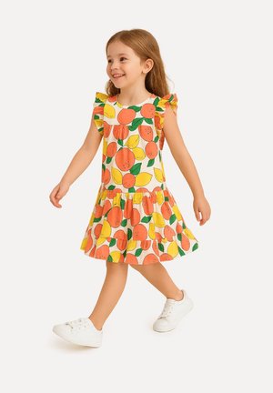 Robe jaune avec des motifs d'orange et de citron, sleeves froncées et jupe évasée, portée avec des baskets blanches.