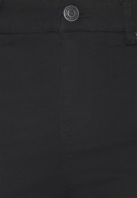 Los jeans de mezclilla negra presentan una textura suave, un cierre frontal con botón y detalles de costura mínimos, centrándose en una silueta ajustada.