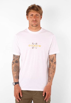 T-shirt en coton blanc avec un logo central "OXBOW" en jaune, entouré de petits motifs de feuilles. Manches courtes, design à col rond.