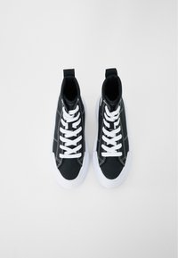 Svarte høyforede sneakers med hvite lisser og gummisåler. Har kontrasterende sømmer og en løftestropp på hælen.