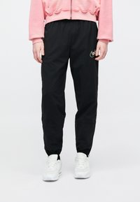Μαύρο παντελόνι jogging με ελαστικές μανσέτες και χρυσή λεπτομέρεια λογότυπου. Κατασκευασμένο από ελαφρύ υλικό, διαθέτει χαλαρή εφαρμογή και πλαϊνές τσέπες.