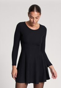 Abito lungo a maniche lunghe nero a costine con corpo aderente e gonna svasata. Presenta un collo rotondo e un tessuto texturizzato.