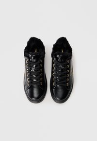 Sorte lær sneakers med falsk pelsfor, gyldne snørehull og en teksturert sidepanel med nagledesign.