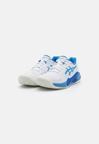 Sapatilhas brancas de desporto com detalhes em azul, parte superior em malha texturizada, sola em borracha e fecho de atacadores. Apresenta um logótipo proeminente ao lado.