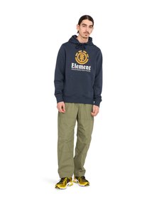 Marineblaues Hoodie mit weißem und goldenen "Element"-Logo, vorderer Tasche, Kapuze mit Kordelzug. Olivgrüne Cargo-Hose mit aufgesetzten Taschen. Gelbe und schwarze Sneakers.