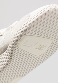 Närbild av en vit Adidas-sneakersula som visar rutmönster och Pharrell Williams logotyp på bågen.