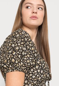 Vestido preto floral com mangas bufantes, decorado com flores brancas e amarelas, tecido texturizado e detalhe de cintura ajustada.