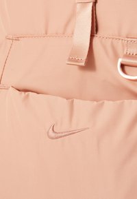 Nike-tas in zachtroze stof, met een gladde textuur, een verstelbare schouderband en een prominent geborduurd logo in een bijpassende kleur.