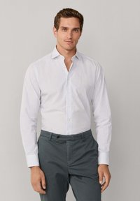 Witte overhemd met een subtiel ruitpatroon, lange mouwen en een klassieke kraag. Gecombineerd met donkergrijze broek.