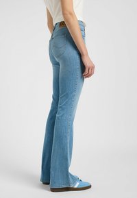 Jeans a campana di un blu chiaro, realizzati in denim, con tasche posteriori, una patch in pelle e una sottile texture scolorita.