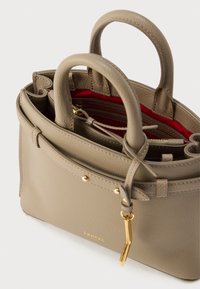 Beežist nahast käekott kahe sangaga, kuldsete metalldetailide ja punase sisevoodriga. Omab struktureeritud disaini ning väikest välist taskut.