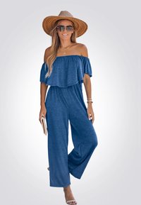 Blauwe off-shoulder jumpsuit met een gelaagd volantontwerp. Gemaakt van zachte stof, met brede benen en gecombineerd met een strohoed en een zonnebril.