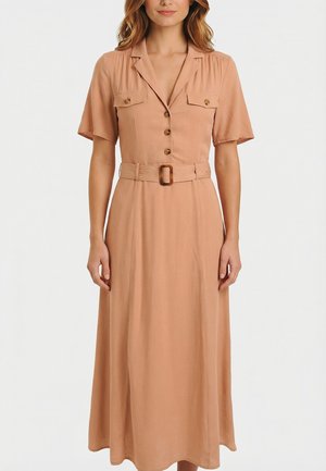 Mujer con un vestido midi color marrón claro, de manga corta, con botones en la parte delantera, dos bolsillos en el pecho con solapas y un cinturón a juego con hebilla.