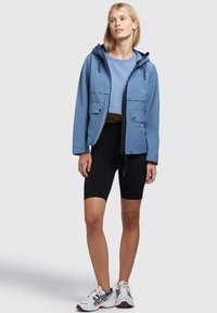 Light blue hooded jacket with two front pockets, paired with a cropped blue top, black bike shorts, and white athletic shoes.