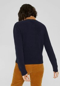Suéter azul marino con dobladillo y puños acanalados, con un color de cuello marrón claro. La tela parece suave con un acabado texturizado.