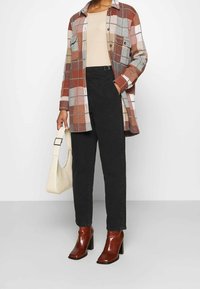 Camisa de cuadros en tonos cálidos, top beige, pantalones de cintura alta negros, botas de tacón marrón y un bolso texturizado color crema.