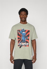 Oliven grøn bomulds T-shirt med et stort blåt og rødt grafik af en superhelt og ordet "SWOOSH" i hvid, kortærmet, rund hals.