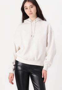 Felpa bianca oversized con cappuccio e logo in rilievo, abbinata a pantaloni in pelle nera fitted. Tessuto morbido e vestibilità rilassata.