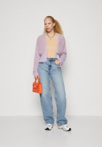 Ceriņkrāsa adīta džempera ar atvērtu priekšpusi, bēšs topiņš, gaiši zili platleņķa džinsi un oranža soma. Iespējamās apavi ir masīvas kedas.