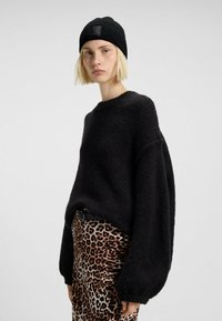 Maglione nero a maglia con finitura testurizzata, maniche larghe e collo rotondo, abbinato a una gonna con stampa leopardata e a un berretto a coste nero.