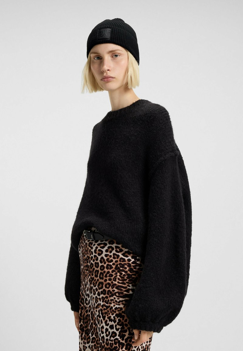 Maglione nero a maglia con finitura testurizzata, maniche larghe e collo rotondo, abbinato a una gonna con stampa leopardata e a un berretto a coste nero.