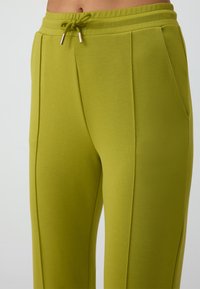 Grüne Jogginghosen mit einem Kordelzugbund, glatter Textur, seitlichen Taschen und dekorativen Nähten an der Vorderseite.
